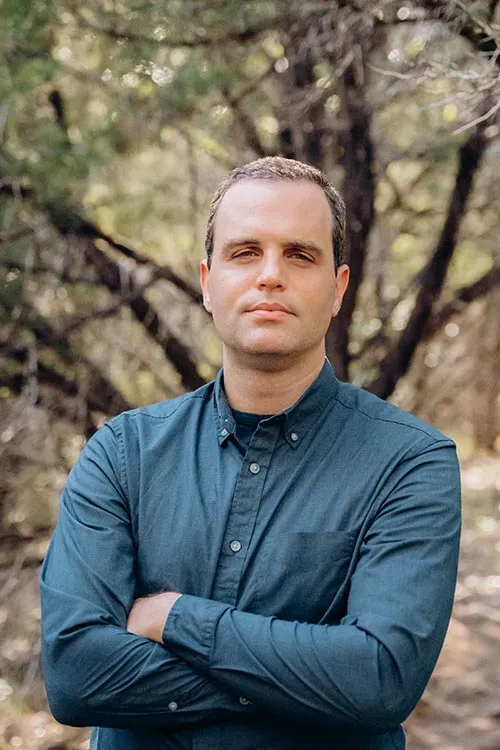 Jason Louv, standing in the woods with arms crossed